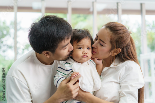 Asian family happy kiss little baby boy in living room at home, young parent and children enjoy love hug standing together.. © ake1150