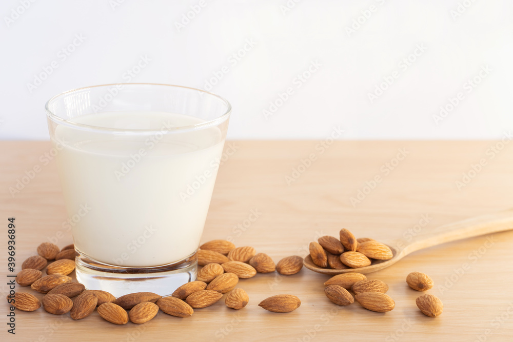 Closeup almond milk in grass and organic raw peeled almond nuts in spoon with laid around cup on wooden background. Closeup almond milk in grass and organic raw peeled almond nuts in spoon with laid around cup on wooden background.