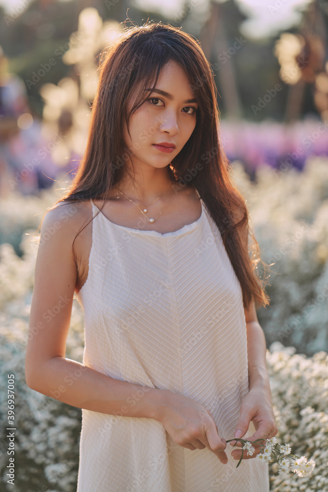 Asian woman in white dress looks directly into the camera while walking in the garden of white flowers