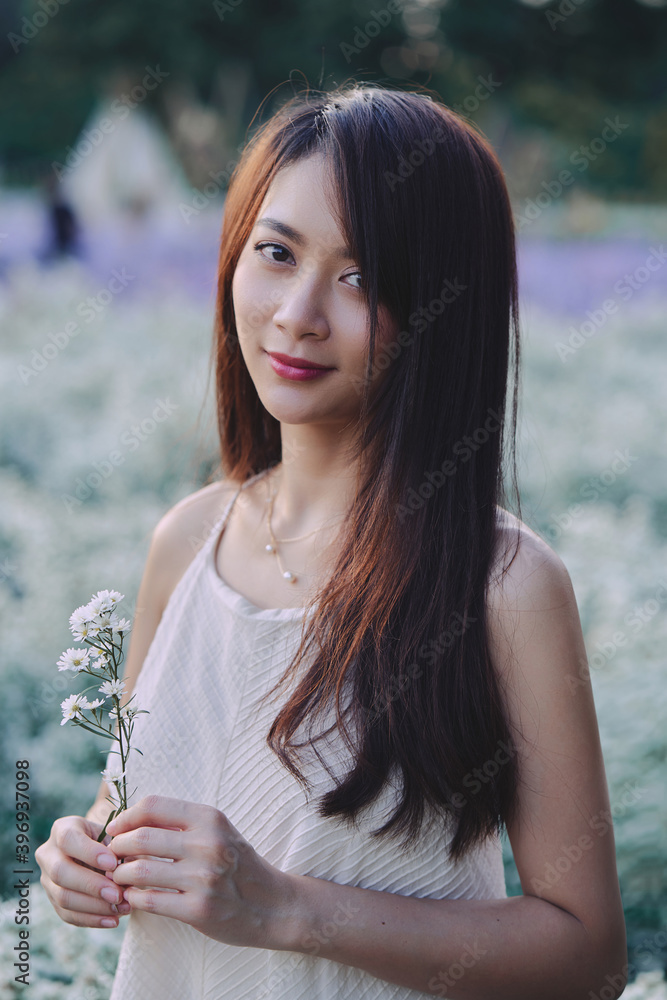 Happy Asian woman in white dress looks directly into the camera while walking in the garden of white flowers