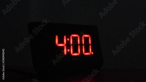 Alarm clock going off at 4:00 AM in dark room. Hand reaches out and stops alarm.