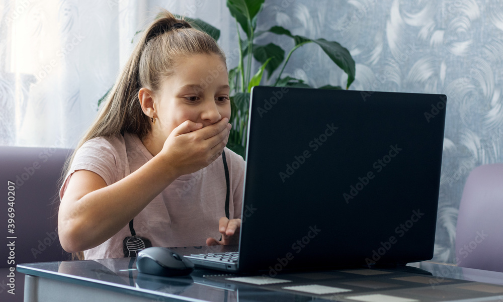 A young schoolgirl sitting at a table is engaged in online training on a laptop during the quarantine period. A young schoolgirl sitting at a table is engaged in online training on a laptop during the quarantine period.