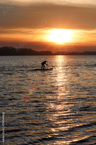 Silhouette of a boy rowing on a SUP (on stand up paddleboard) at sunset in a winter river