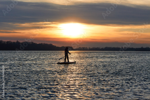 Silhouette of a boy rowing on a SUP (on stand up paddleboard) at sunset in a winter river