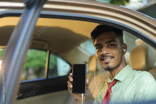 Young indian business man or employee sitting in car and showing mobile screen