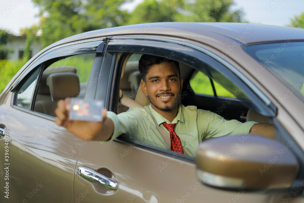 Young indian businessman or employee sitting in car and showing card Young indian businessman or employee sitting in car and showing card