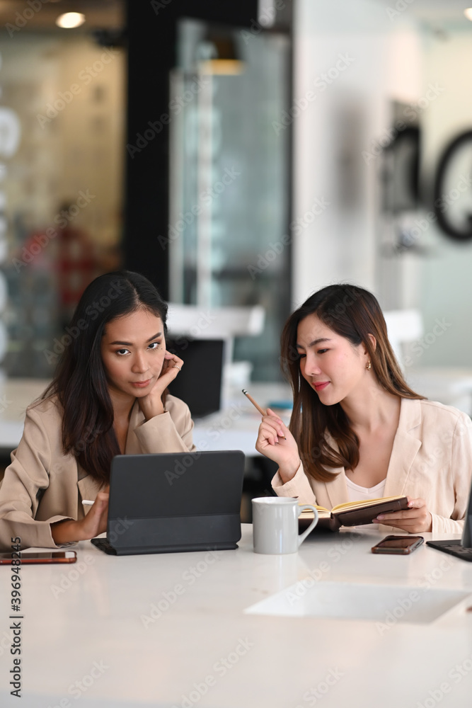 Two businesswomen are collaborating and discussing project plans while using a digital tablet in the office. Two businesswomen are collaborating and discussing project plans while using a digital tablet in the office.
