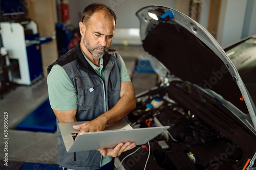 Car mechanic using laptop while running engine diagnostic at repair shop.