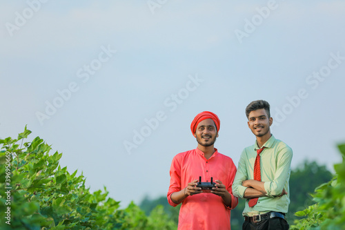 Young indian farmer holding remote in hand and control flying drone with agronomist at agriculture field