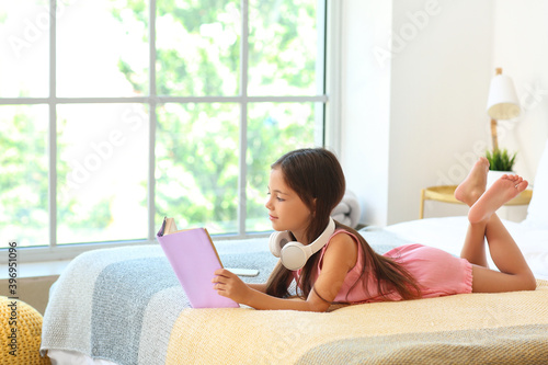 Cute little girl with headphones reading in bedroom photo
