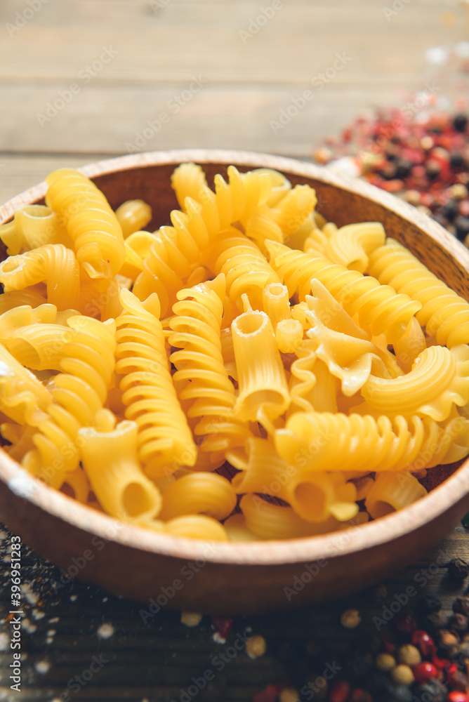 Bowl with different uncooked pasta on wooden background Bowl with different uncooked pasta on wooden background