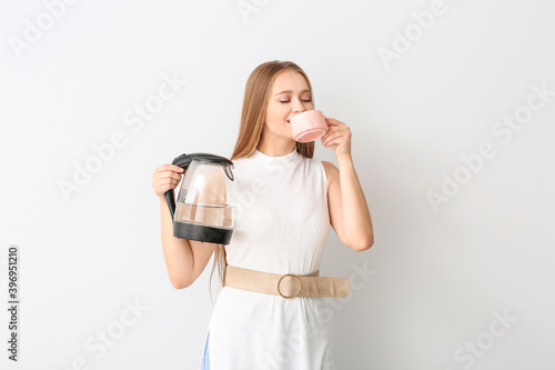 Happy woman holding electric kettle and drinking tea on white background