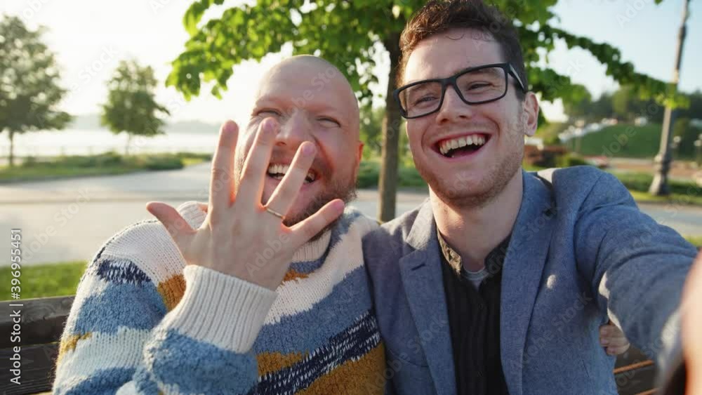 Sefie portrait of young gay couple feeling happy showing ring. LGBTQ men smile to camera. A guy make proposal of mariage to his boyfriend. LGBTQI, Pride Event, LGBT Pride Month, Gay Pride Symbol