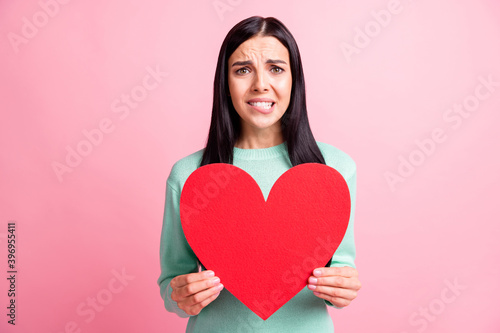 Photo portrait of woman biting lower lip holding big red heart postcard isolated on pastel pink colored background © deagreez