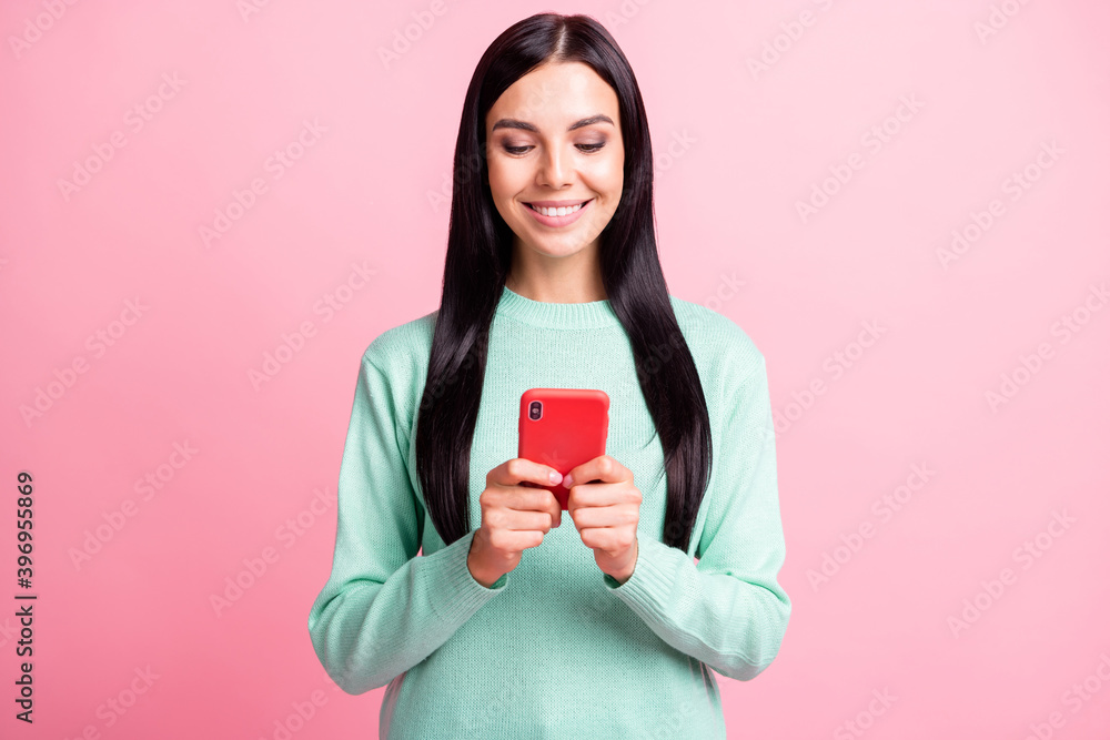 Photo portrait of woman holding phone with two hands typing isolated on pastel pink colored background Photo portrait of woman holding phone with two hands typing isolated on pastel pink colored background
