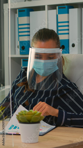 Businesswoman with visor and protection mask working in new normal business office. Freelancer discussing with colleague in financial company respecting social distance during global pandemic.