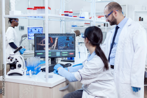 Group of scientist analysing genetic material. Team of researchers doing pharmacology engineering in sterile laboratory for healthcare industry with african assistant in the background.