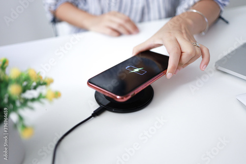 Charging mobile phone battery with wireless charging device in the table. Smartphone charging on a charging pad