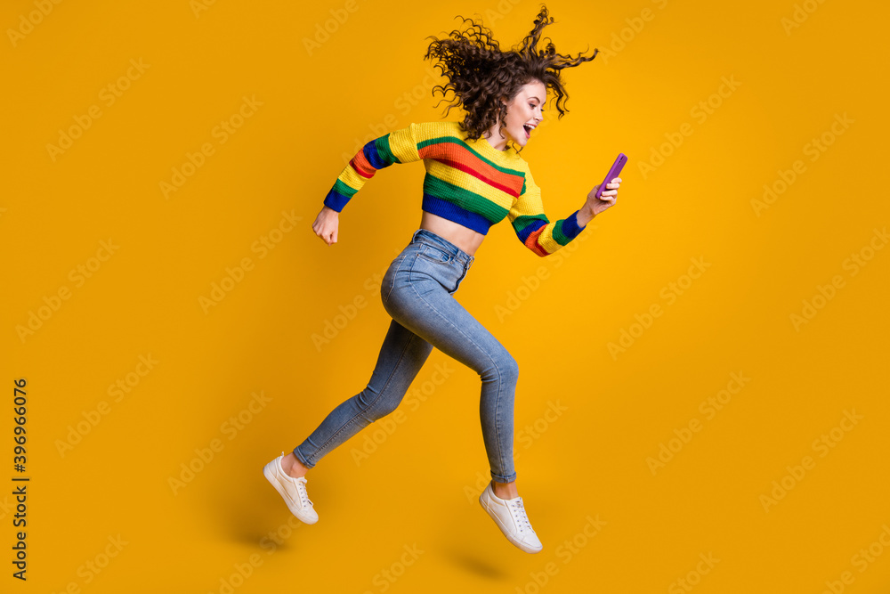 Profile full size photo of cheerful pretty wavy hair girl run read message wear sweater jeans sneakers isolated on yellow background
