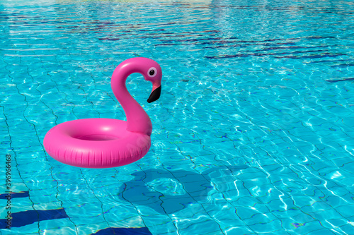 Summer concept background. Pink inflatable flamingo in pool water for summer beach background. Pool float party. © Maksym