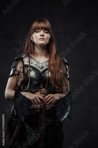 Portrait of pretty and at the same time dangerous nordic female fighter holding huge axe in dark background.