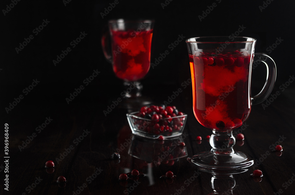 Red fruit tea with cowberry, blueberry in two transparent glasses on black wood table in dark interior, copy space. Red fruit tea with cowberry, blueberry in two transparent glasses on black wood table in dark interior, copy space.
