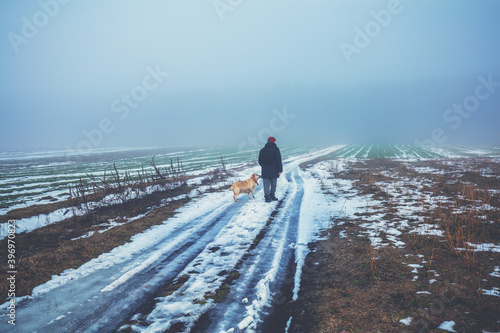 Man with Labrador retriever dog walking in the countryside in winter. Fields covered with the first snow