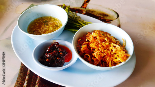 Close up side dish of oyster or shell with chili paste, fried onion, acacia shoots and Thai spicy and sour sauce in blue dish or plate at seafood restaurant. Asian food