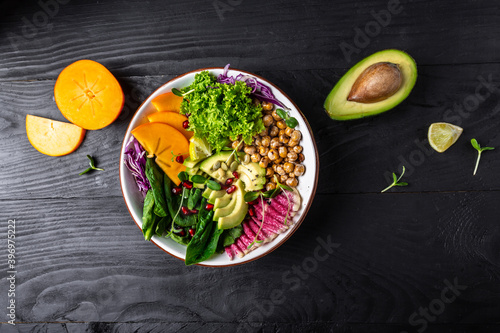 Buddha bowl, healthy and balanced food. roasted chickpeas, avocado, persimmon, spinach, avocado, watermelon radish and seeds. top view