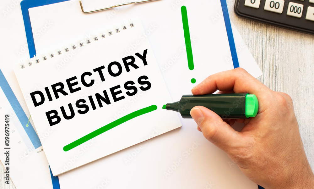 A hand with a marker writes the text DIRECTORY BUSINESS in a notebook on the desktop. Top view. A hand with a marker writes the text DIRECTORY BUSINESS in a notebook on the desktop. Top view.