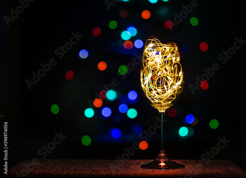 Crystal wine glasses with golden glowing garland on Christmas table bokeh light background. Festive screensaver. Romantic New Years eve dinner champagne couple in love.Magic winter holidays atmosphere