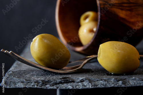 Green olive presented on a fork on a slate background