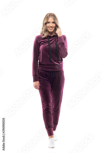 Beauty young woman in burgundy plush sweatsuit and socks walking and smiling at camera. Full body length isolated on white background. 