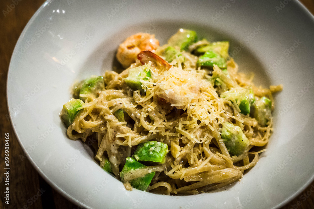 spaghetti with avocado, shrimp, seafood and parmesan on top served in a white bowl