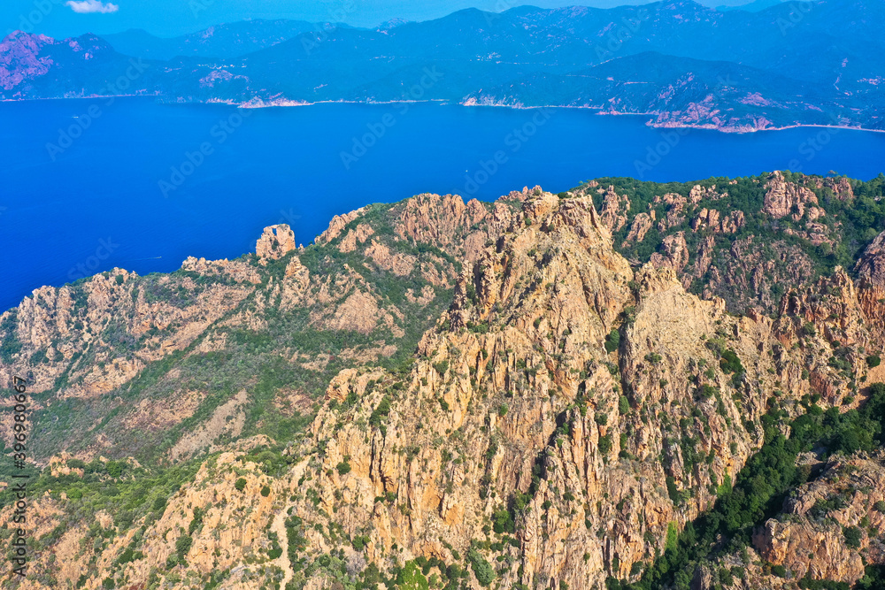 Aerial view of beautiful view of sunlit red mountains and the Mediterranean Sea with the Bay of Porto in Calanches area on Corsica island