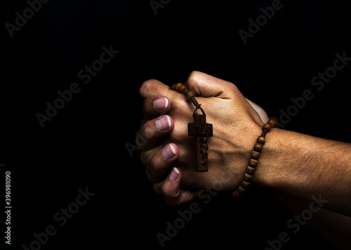 Woman's hands holding a wooden rosary and praying