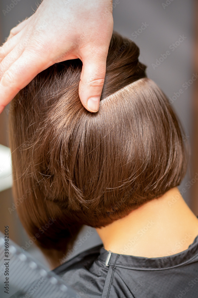 Naklejka premium Hairdresser checks short brown hairstyle of a young woman in a beauty salon