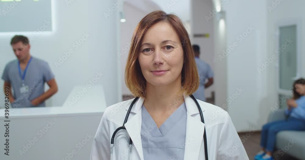 Close up portrait of Caucasian beautiful female doctor with stethoscope standing in clinic at reception, looking and smiling at camera. Woman medical practitioner at work. Healthcare concept Close up portrait of Caucasian beautiful female doctor with stethoscope standing in clinic at reception, looking and smiling at camera. Woman medical practitioner at work. Healthcare concept