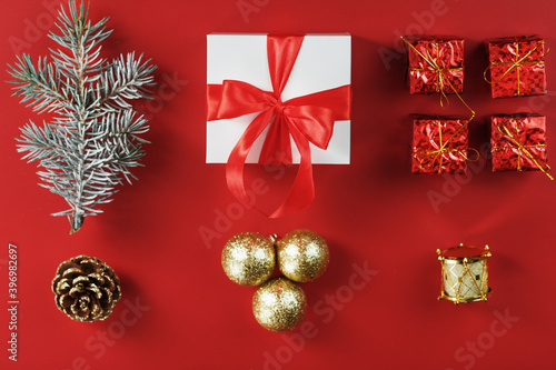 White box with a gift and a red bow, around Christmas decorations with fir branches on a red background