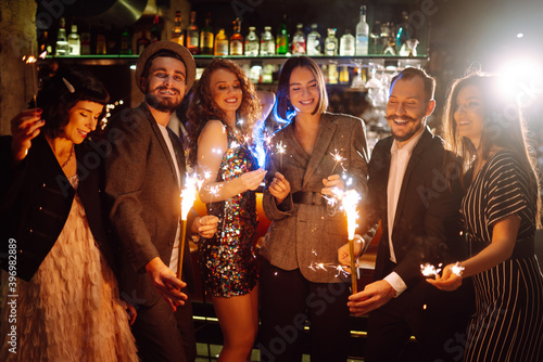 Friends celebrate Christmas or New Years party with sparklers and champagne. Group of happy people enjoying party with fireworks.Winter holiday, youth, lifestyle concept.