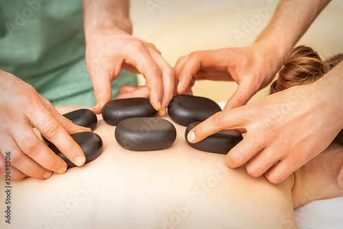 Two massage therapists putting spa stones on the female back in the spa salon