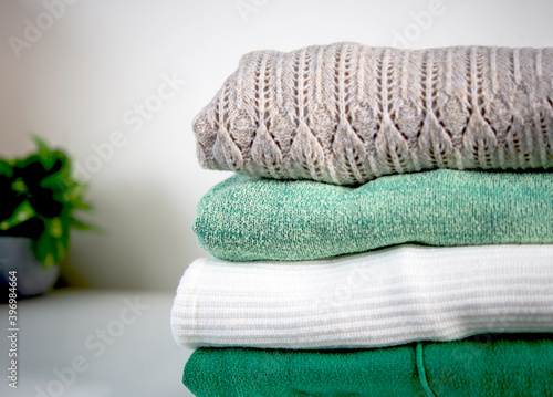 Stack of cozy knitted sweaters pastel tone green and white on a white table. Retro style. Warm concept