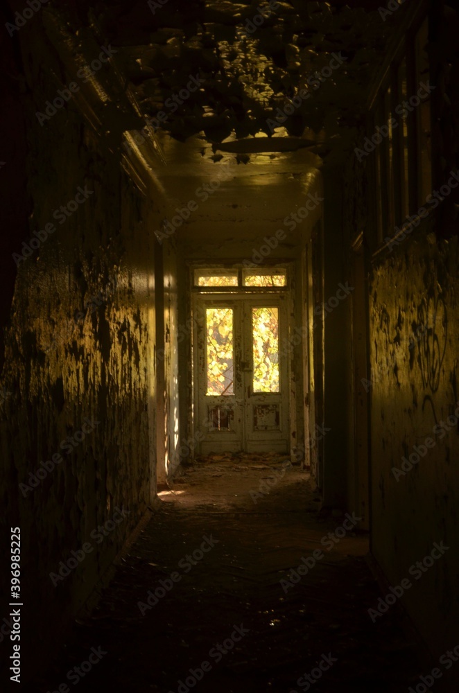 A long corridor, in an old, abandoned building, in the distance, a window through which sunlight enters.