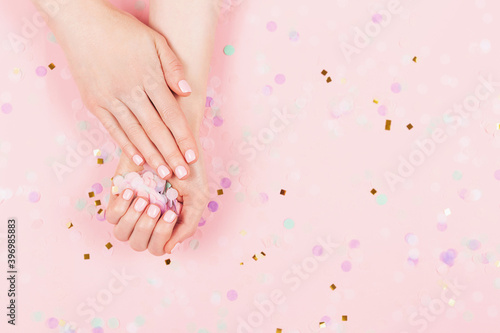 Manicure and nail care concept. Woman hands are holding pastel confetti. Perfect pastel pink nail polish. Party  holidays or celebration vibes.