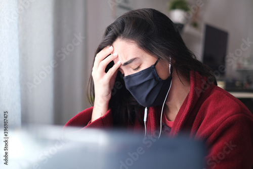 A woman wearing a black mask trying to stay focused while working from home due to Covid-19, struggling with anxiety and depression. Mental illness awareness