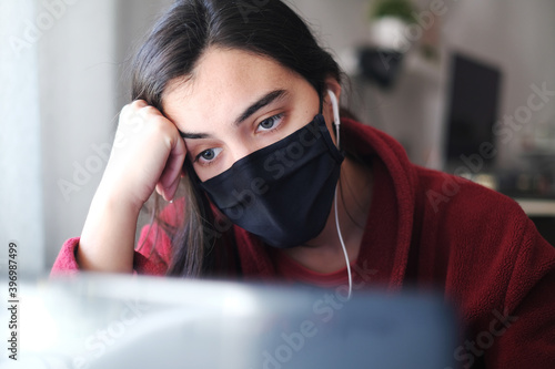 A woman wearing a black mask trying to stay focused while working from home due to Covid-19, struggling with anxiety and depression. Mental illness awareness