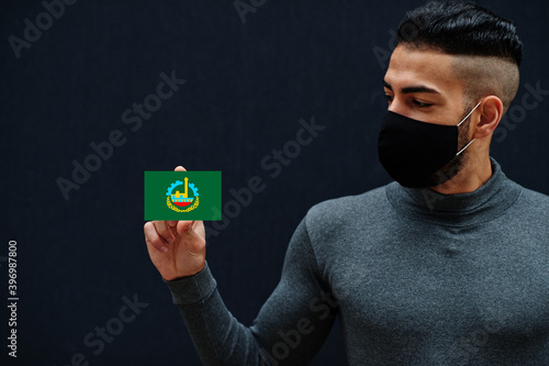 Egyptian man in gray turtleneck and black face protect mask show Qalyubia flag isolated background. Governorates of Egypt coronavirus concept. photo