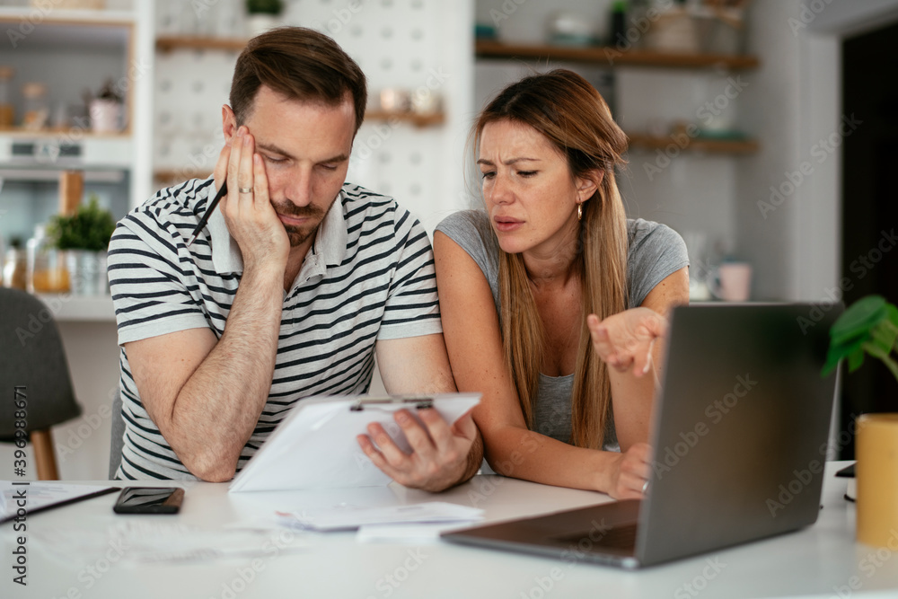 Worried couple paying their bills online with laptop at home in the living room. Couple having financial problems.. Worried couple paying their bills online with laptop at home in the living room. Couple having financial problems..