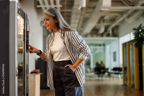Happy white-haired mature woman using vending machine and smiling