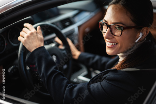 Tablou canvas Beautiful happy businesswoman in earphones and eyeglasses driving car